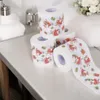 Several rolls of toilet paper with a Christmas Santa Claus motif are stacked on a white surface, with bathroom accessories in the background. Náhľad obrázku produktu