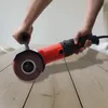 A person is using a red and black power tool with a brush attachment on a wooden surface. Podgląd zdjęcia produktu