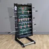 A foosball table is shown in a room with a gray wall and wooden floor. Produktbild-Vorschau
