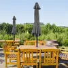 An outdoor patio scene with wooden tables and chairs, and two closed gray umbrellas. Produktbild-Vorschau