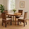 A dining set with a round wooden table and four wicker chairs with beige cushions, placed on a round jute rug in a well-lit room with a large window. Produktbild-Vorschau