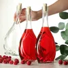 Three glass bottles with cork stoppers, two filled with red liquid and one empty, are arranged on a wooden surface with raspberries and eucalyptus leaves. Voir les images du produit