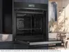 An open built-in oven in a modern kitchen setting, with a dining area visible in the background. Produktbild-Vorschau