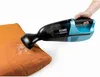 A hand is holding a blue and black handheld vacuum cleaner and using it to clean a small orange cushion. Produktbild-Vorschau