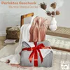 A cozy scene with blankets draped over a chair and a bench, with a gift-wrapped blanket in the foreground. Náhled obrázku produktu