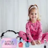 A young girl in pink pajamas is sitting on a bed with a makeup set. Produktbild-Vorschau