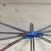A close-up view of a measuring tool with multiple metal arms radiating from a blue central hub, set against a light-colored wooden background. Náhľad obrázku produktu