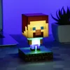 A Minecraft Steve Icon Light is displayed on a desk with a laptop and a plant in the background. Produktbild-Vorschau