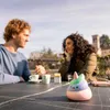 Two people sitting at a table outdoors, with a small toy in the foreground. Voir les images du produit