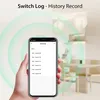 A hand holding a smartphone displaying a switch log, with a blurred background of a dining area and decorative lighting. Náhled obrázku produktu