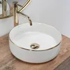 A close-up shot of a white basin with a gold rim and a gold faucet, placed on a wooden surface. Produktbild-Vorschau