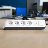 A power strip with four outlets and a switch sits on a wooden desk in an office environment. Náhľad obrázku produktu
