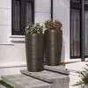 Two large brown rain barrels filled with flowers are placed on a stone staircase next to a modern house. Produktbild-Vorschau
