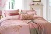 A beautifully made bed with pink floral bedding and decorative pillows, set in a bright, airy bedroom with a fireplace in the background. Produktbild-Vorschau