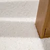 A close-up view of a fluffy white rug with a wooden furniture leg on the right side. Produktbild-Vorschau
