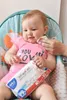 A baby sitting in a high chair, being wiped with a wet wipe. Voir les images du produit