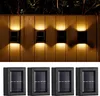 Four solar-powered wall lights are shown mounted on a wall, with their lights illuminating the wall and casting shadows. Below them, four individual solar panels are displayed. Produktbild-Vorschau