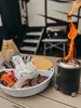A s'mores making setup with a portable fire pit and ingredients arranged on a tray, with an RV in the background. Voir les images du produit