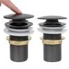 Two pop-up drain assemblies are shown side-by-side against a white background. A finger is pressing down on the top of the left assembly. Produktbild-Vorschau