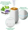 A white aroma diffuser with a wooden top, emitting steam, surrounded by images of mint, lime, lavender, and vanilla beans, and close-ups of its control panel and LED light. Náhľad obrázku produktu