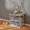A white shelving unit with clear storage boxes filled with shoes and other items, placed on a wooden floor next to a gray wall. Produktbild-Vorschau