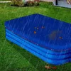 A blue pool cover is on a grassy lawn during a rain shower, with some leaves on the cover. Produktbild-Vorschau