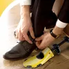 A person is shown adjusting their shoe, with a shoe stretcher in the foreground. Podgląd zdjęcia produktu