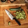 A chef's knife is shown on a cutting board with sliced cucumbers. Podgląd zdjęcia produktu