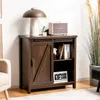 A dark brown wooden sideboard cabinet with a sliding barn door and an open shelf displaying books and a digital clock. A lamp and a speaker are on top of the cabinet. Podgląd zdjęcia produktu