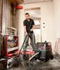 A man is using a wet/dry vacuum cleaner on a wet floor in a room under construction. Podgląd zdjęcia produktu