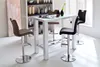 A modern dining set with a white table and four bar stools in a bright room. Voir les images du produit