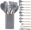 A set of 12 gray silicone kitchen utensils with wooden handles, neatly arranged in a gray holder on the left, and a separate display of the same utensils lined up on the right. Náhľad obrázku produktu