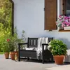 A black wooden garden bench with storage is placed on a paved patio next to potted plants and flowers. Anteprima dell’immagine prodotto