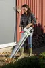 A woman is using a leaf blower in a yard next to a building. Produktbild-Vorschau