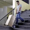 A man is using a hand truck to move a large box up a set of stairs. Náhled obrázku produktu
