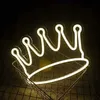 A white neon crown light sits in a wire basket with a yellow object behind it. Produktbild-Vorschau