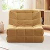 A yellow floor chair with a tufted design is placed on a white rug in a room with a window and wooden cabinets in the background. Náhled obrázku produktu