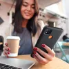 A woman is sitting at a table with a laptop and a coffee cup, holding a phone with a case. Anteprima dell’immagine prodotto