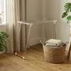 A narrow drying rack is shown in a room with a window and curtains, next to a basket of folded towels. Produktbild-Vorschau