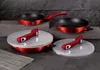 A set of red pots and pans with black interiors and red handles, along with clear lids, are arranged on a dark surface with a stone-like background. Produktbild-Vorschau