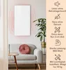 A white infrared heater is mounted on a wall above a gray sofa in a living room setting. Decorative elements like a plant and a round cushion are visible. Podgląd zdjęcia produktu