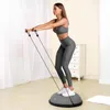 A woman is exercising on a balance trainer with resistance bands in a room. Anteprima dell’immagine prodotto