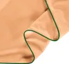 A close-up view of a folded peach-colored fabric with a green trim. Produktbild-Vorschau