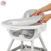 A person's hands are shown attaching a tray to a high chair. Podgląd zdjęcia produktu