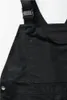 A close-up view of a black bib overall, focusing on the chest pocket and strap buckle. Produktbild-Vorschau