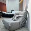 A modern living room setting with a grey sofa in the foreground and a black couch in the background. Produktbild-Vorschau