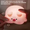 A hand is touching a cute, glowing pig-shaped night light. Podgląd zdjęcia produktu