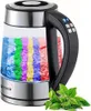 A glass electric kettle with colored water inside, sitting next to a sprig of green tea leaves. Produktbild-Vorschau