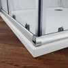 A close-up view of the corner of a modern shower enclosure, showing the chrome trim and glass panels resting on a white shower tray, with a wooden floor visible below. Produktbild-Vorschau
