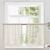 Two sheer cream-colored cafe curtains with tassels hanging on a window. Anteprima dell’immagine prodotto